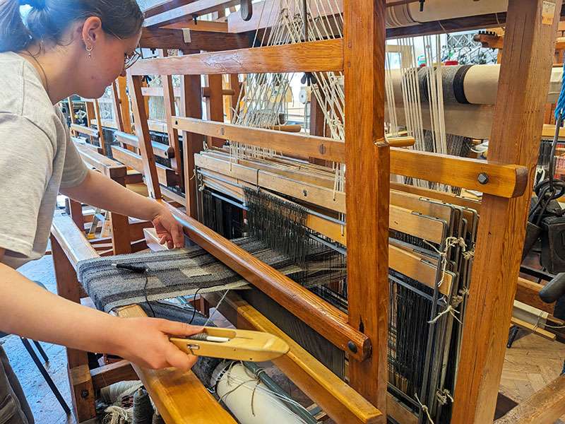 A photo of me weaving at a dobby loom.
