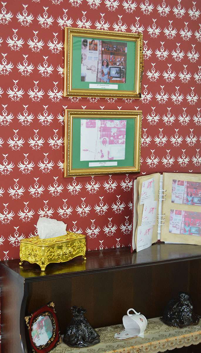 Detailed image of red flock wallpaper, where each pattern is comprised of birds. The wallpaper is behind a Glass Cabinet and gold frames.